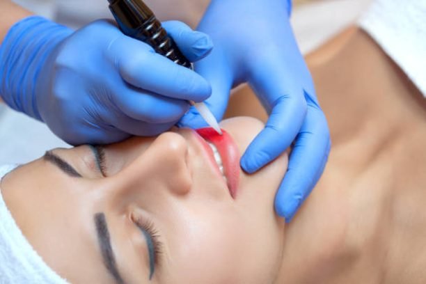 Permanent make-up for lips of beautiful woman in beauty salon. Closeup beautician doing lip tattooing. Face close-up. Make-up and Cosmetology concept.