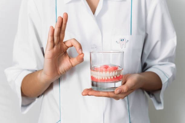 An orthopedic dentist shows how to take care of dentures, close-up. Dental implant care. A complete removable denture in the hands of a doctor. Oral hygiene. Copy space