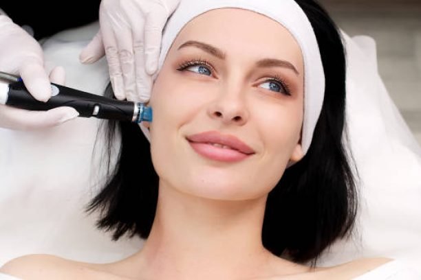 Cosmetology clinic. Professional female cosmetologist doing Hydradermabrasian procedure while being a work. Attractive nice woman lying on the medical bed while having beauty procedures