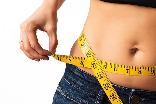 Woman measuring her waistline with yellow measuring tape.