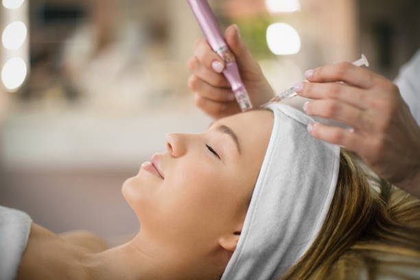 Unrecognizable beautician performs facial treatment on a young woman at beauty salon.