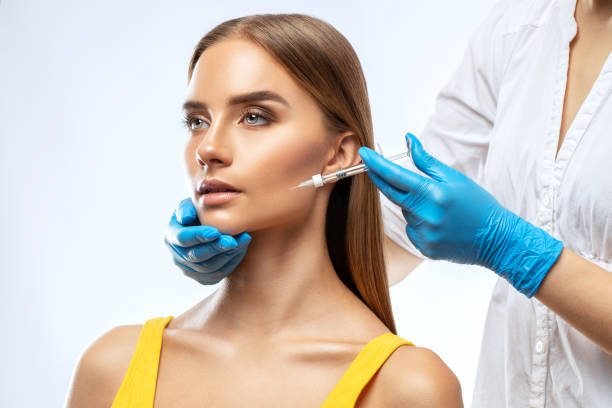 Cosmetologist makes rejuvenating anti wrinkle injections on the face of a beautiful woman in a yellow blouse. Female aesthetic cosmetology in a beauty salon.